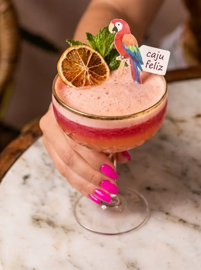 Drinque Caju Feliz na taça com enfeite de papagaio