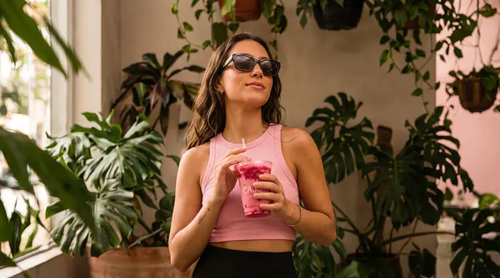 Mulher entre plantas segurando bebida Caju